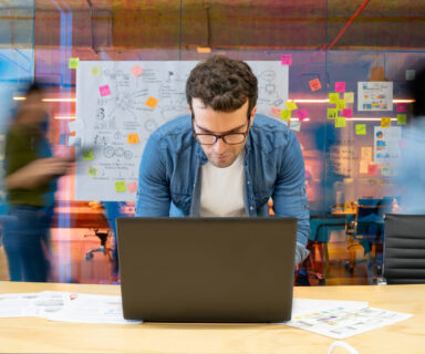 Man working at a creative office using his computer and people moving at the background